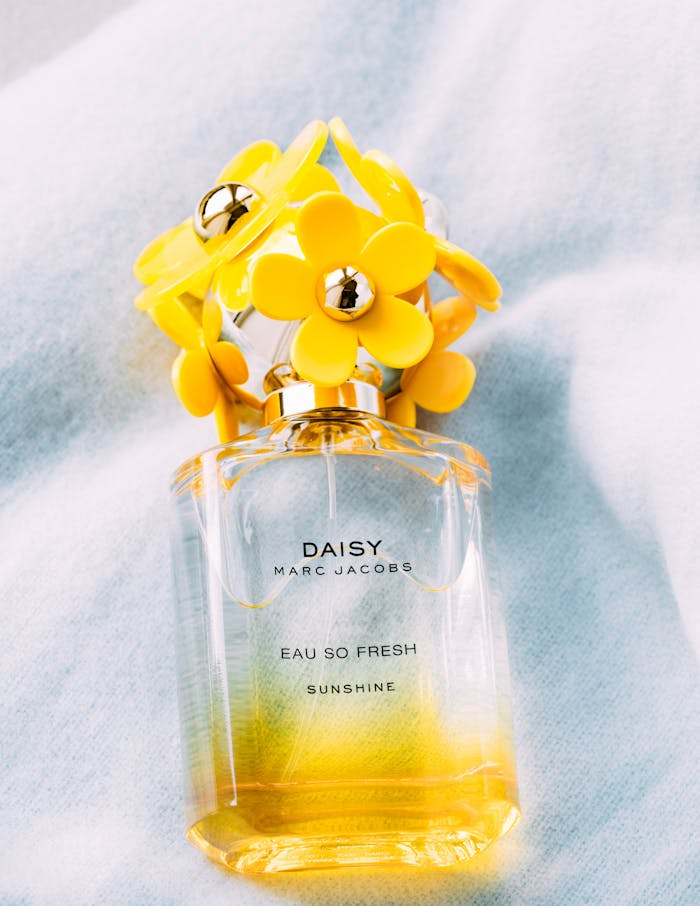 Vibrant yellow floral-themed Daisy perfume bottle on soft cloth background.
